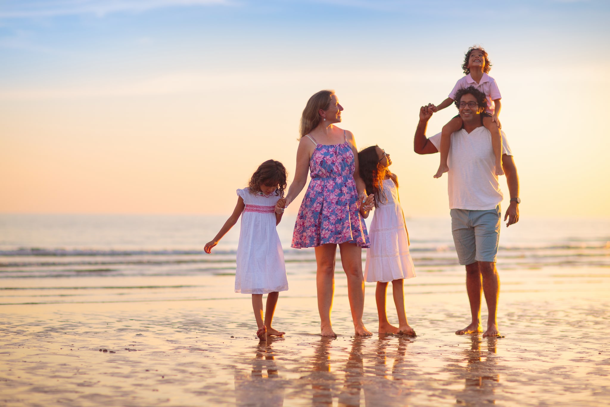 Family with kids walking on tropical beach at sunset. Cute little kids running with parents. Travel with kid. Summer vacation on sea shore. Family holiday with children. Water sport fun.