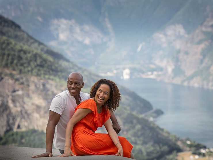 Couple sitting on a rock and smiling with their backs to a mountainous coastline