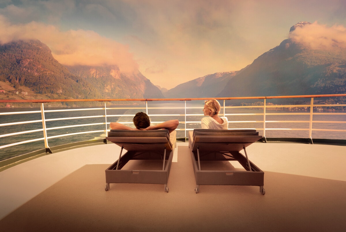 Two people on the front of a cruise ship infront of mountains