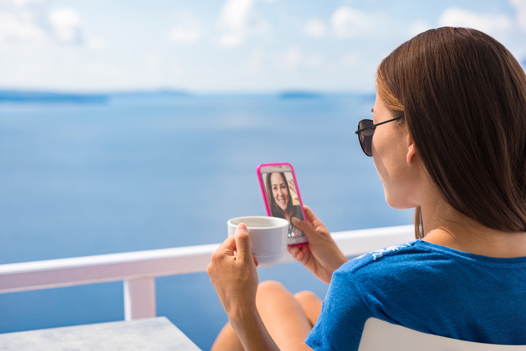 Phone morning breakfast woman drinking coffee cup on Europe summer vacation relaxing girl at cafe reading cellphone at outdoor terrace view of Ocean in Santorini, Greece. European destination holiday.
