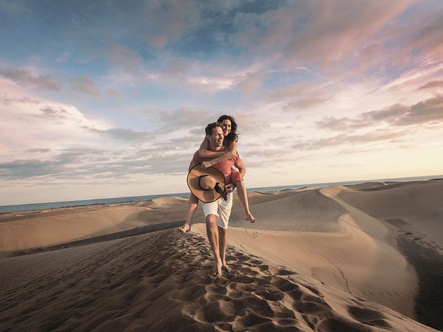 {"metadata_en_GB":{"alt-text":"Man giving woman piggy back in sand dunes"},"metadata_en_AU":{"alt-text":"Man giving woman piggy back in sand dunes"}}