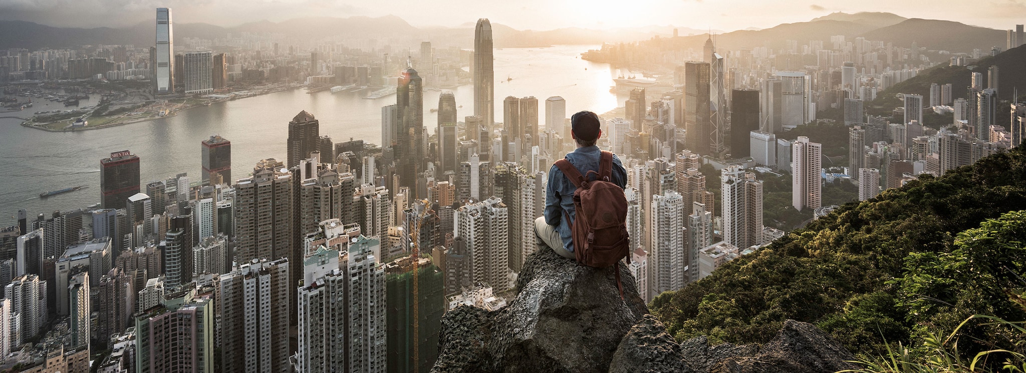 {"metadata_en_GB":{"alt-text":"Asia, China, Hong Kong, man sitting on rock in front of Hong Kong skyline at sunrise"}}