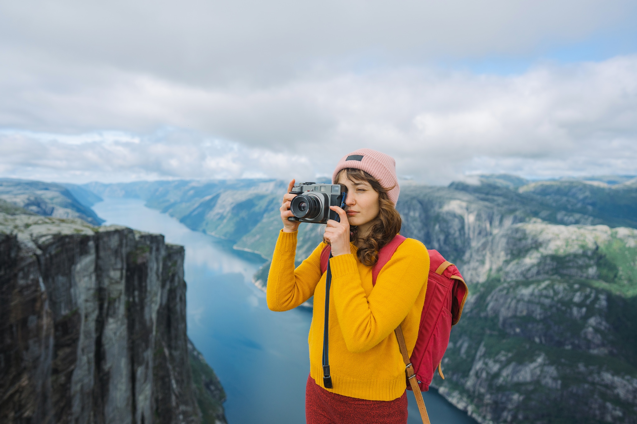 Woman in yellow and red outfit photographing Lysefjorden from Kjerag mountain