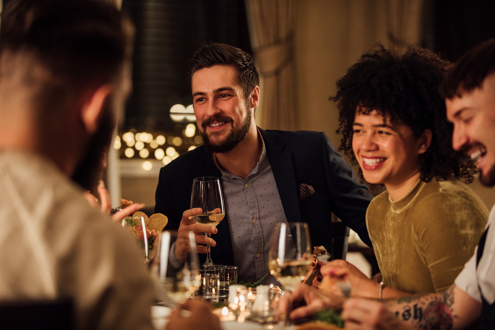 Group of friends are enjoying a meal in a restaurant. They are are talking and laughing while eating and drinking wine.