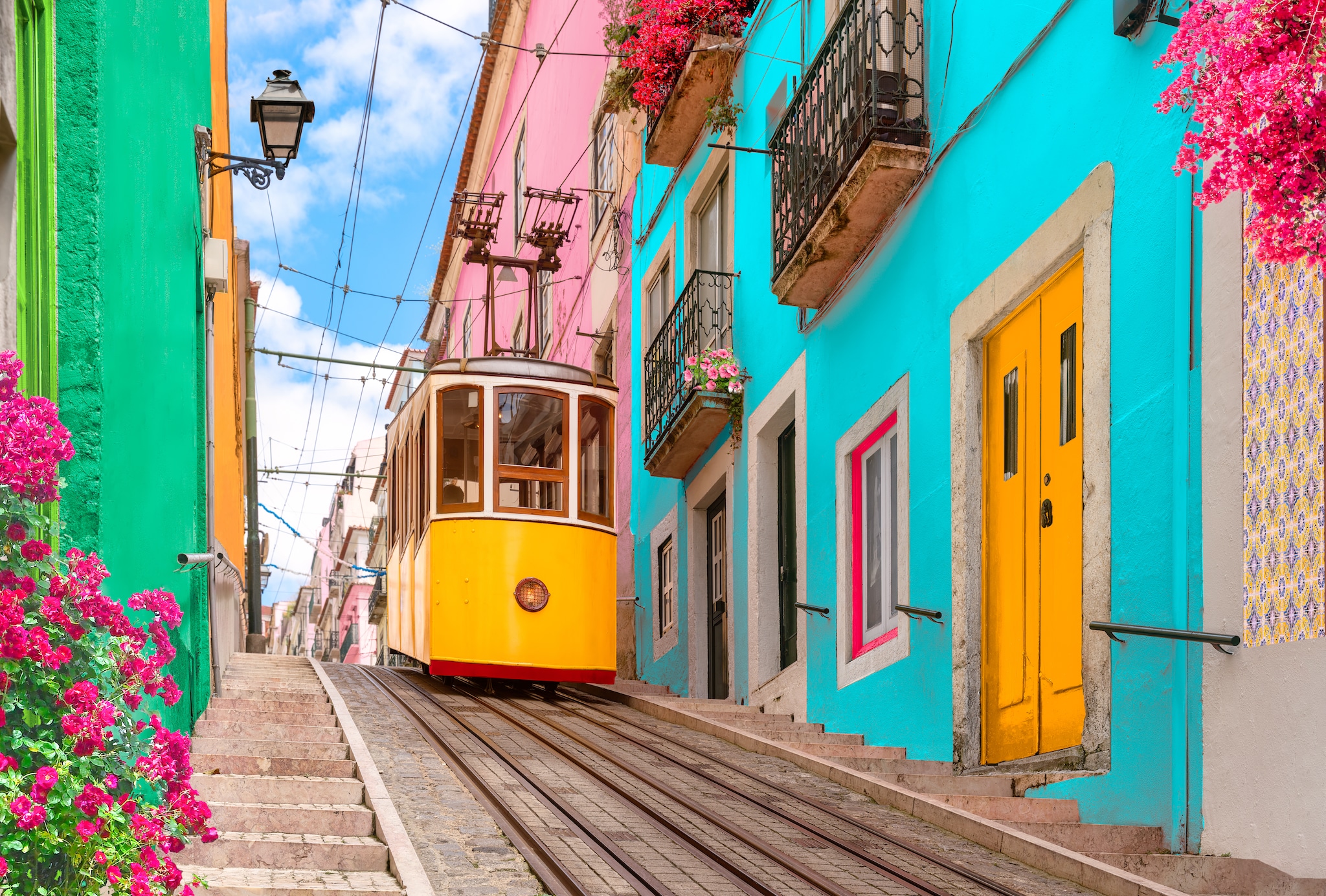 {"metadata_en_GB":{"alt-text":"Yellow typical tram on a street with colorful houses and flowers on the balconies - Bica Elevator going down the hill of Chiado in Lisbon, Portugal."}}